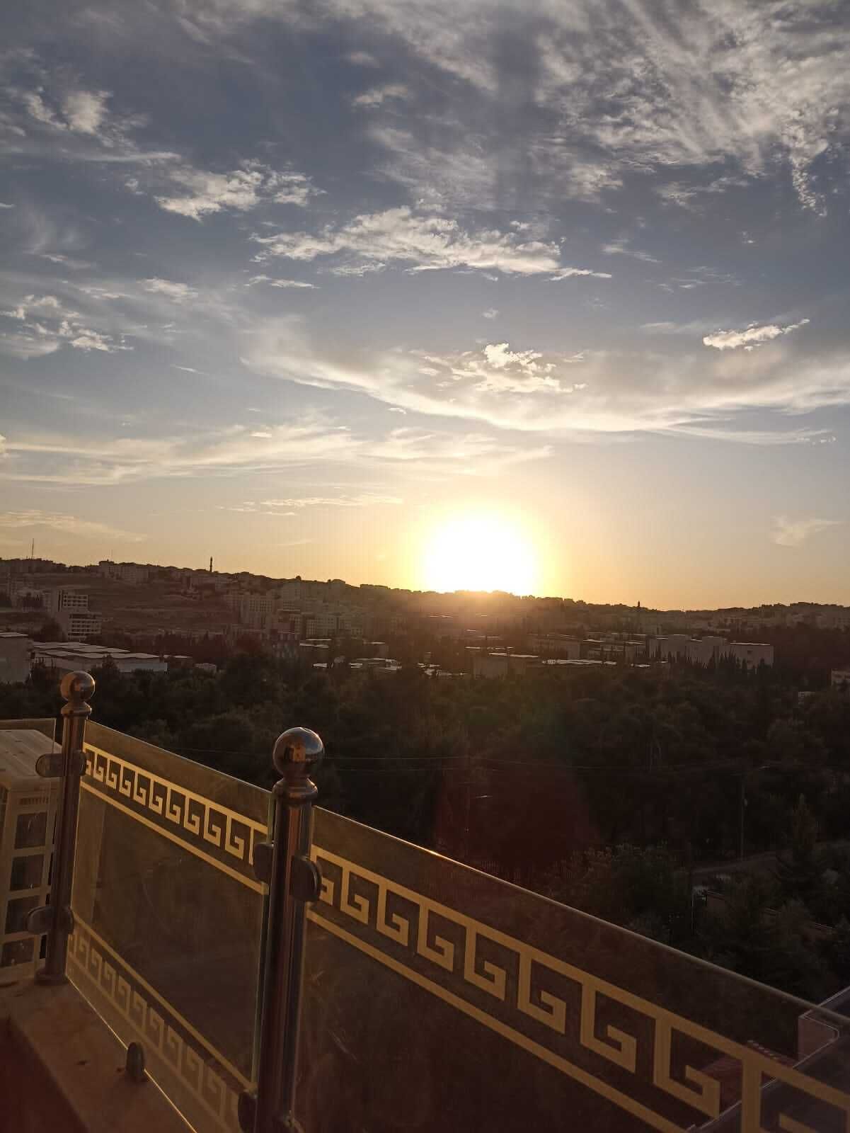 Ein Balkon mit dekorativer Geländer und Blick auf eine Stadtlandschaft im Abendrot.