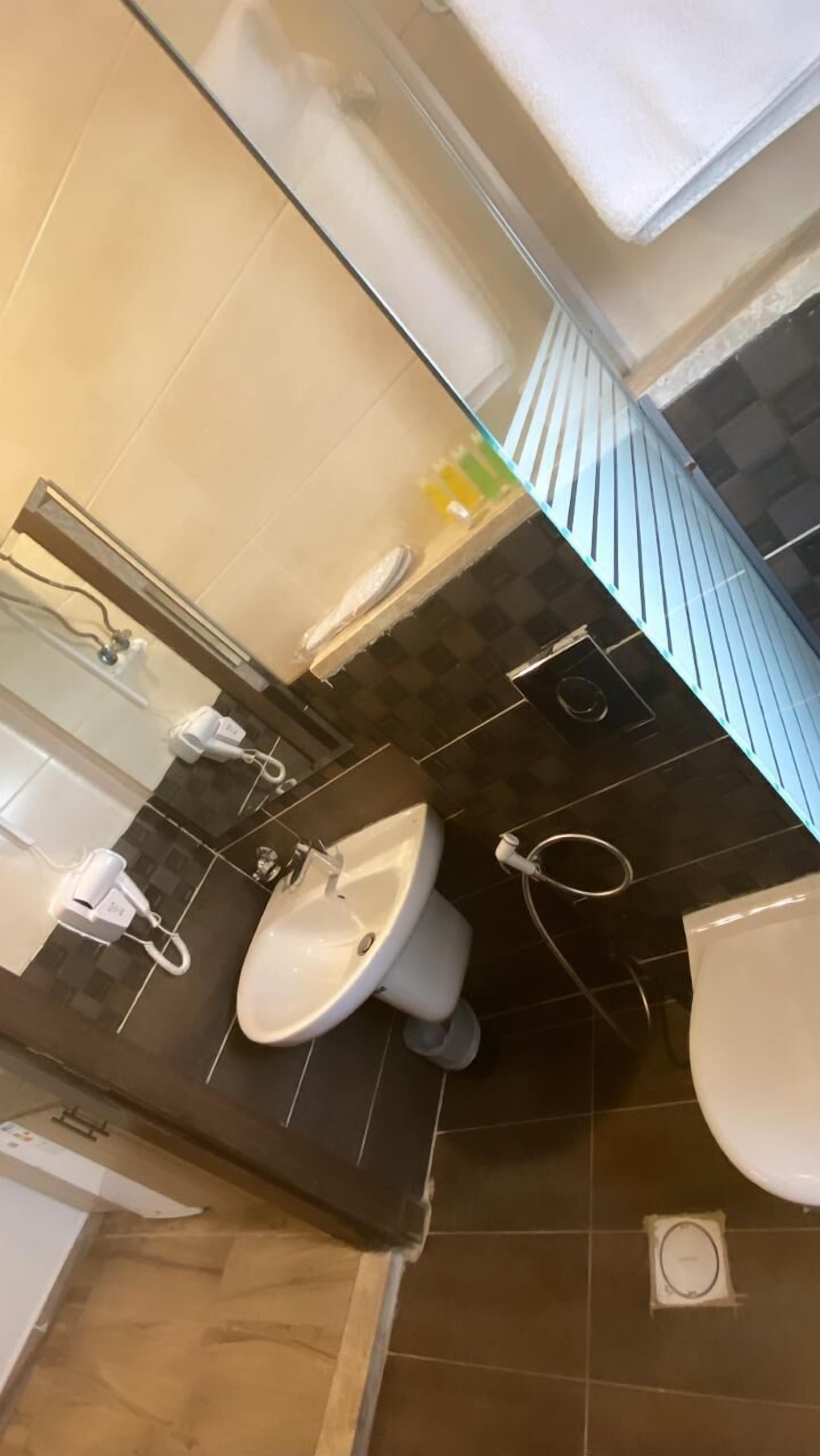 A bathroom with a sink, mirror, and towel rack. The walls are tiled in a checkered pattern of dark and light tiles.