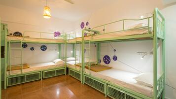 A dormitory room with bunk beds, a ceiling fan, and wall clocks.