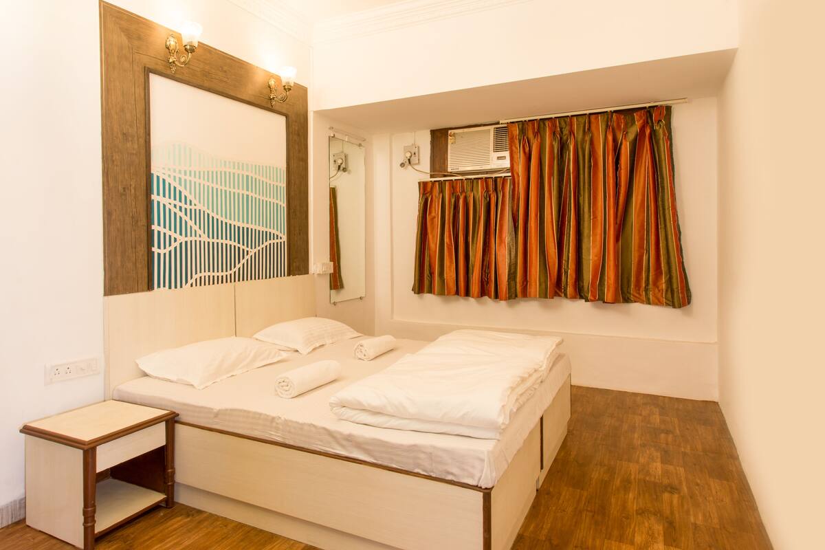 Ein Hotelzimmer mit einem Bett, einem Nachttischchen, einem Spiegel und einem Fenster mit Vorhängen.