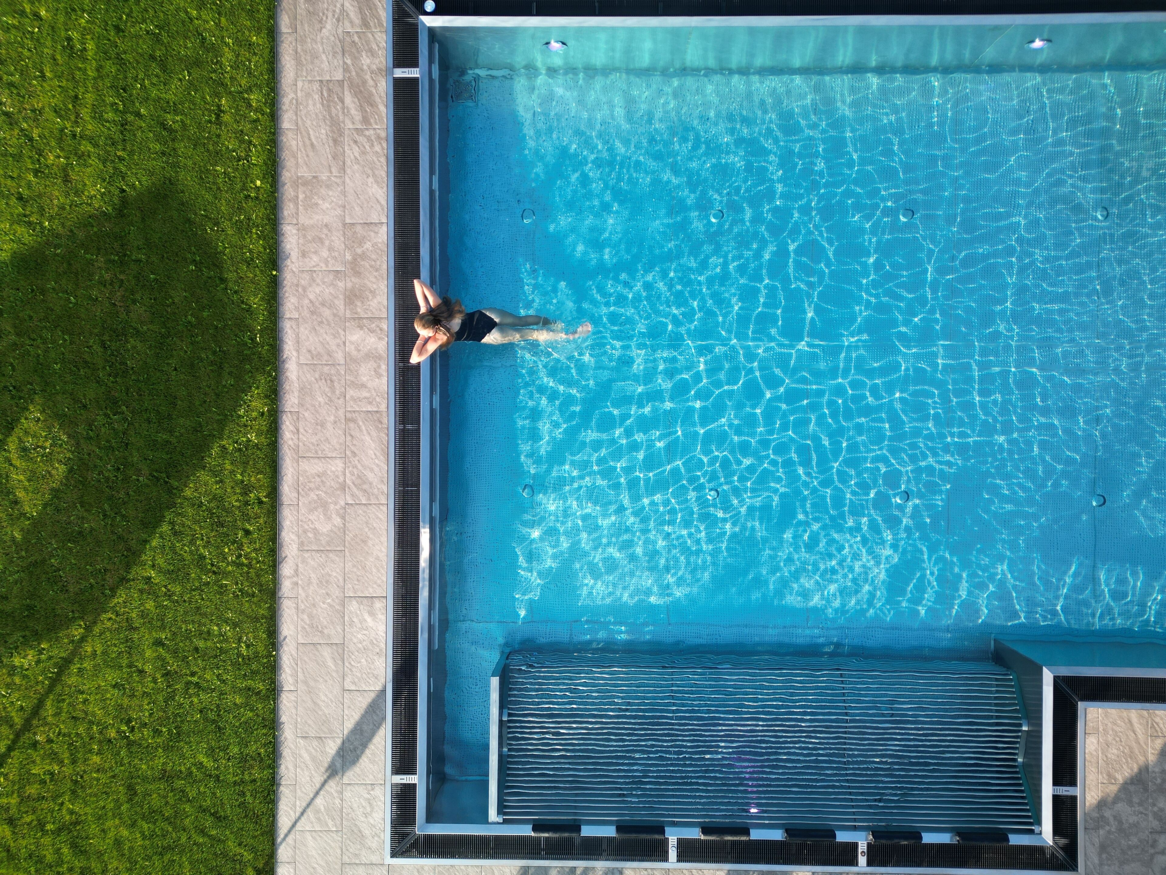 Vista aérea de una piscina rectangular con agua cristalina, rodeada por una terraza de baldosas y una zona ajardinada.