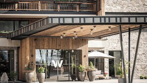 Un edificio moderno con fachada de madera, grandes plantas en macetas y un área de entrada cubierta.