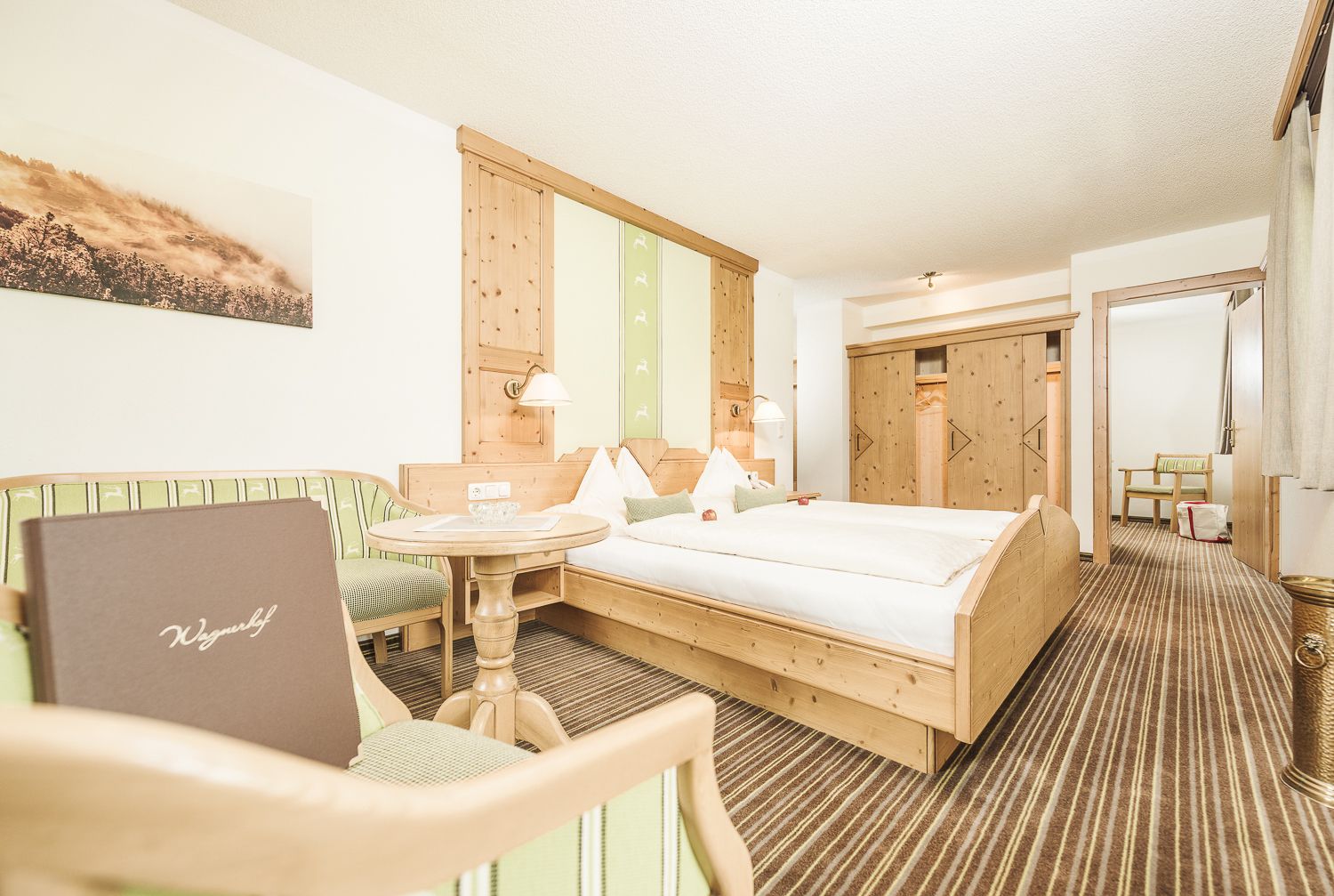 A hotel room with a bed, a small table, a chair, a desk, and a wardrobe.