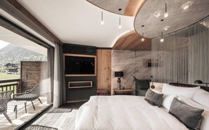 Un dormitorio con una cama grande, televisor, cabecera de madera y vistas a las montañas.