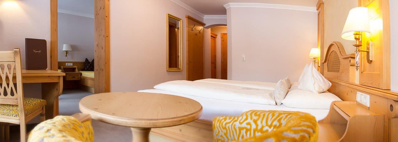 A hotel room with a bed, a round table, a chair, and a small desk with a lamp.