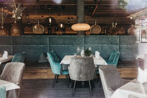 Interior de restaurante con sillas color turquesa, techo de madera, lámparas colgantes y pared con textura.