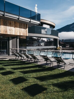 Un edificio moderno con zona de piscina, sillas de descanso y una estatua en el balcón.
