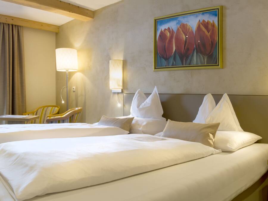 A hotel room with two beds, a painting of tulips, a desk, and a chair.