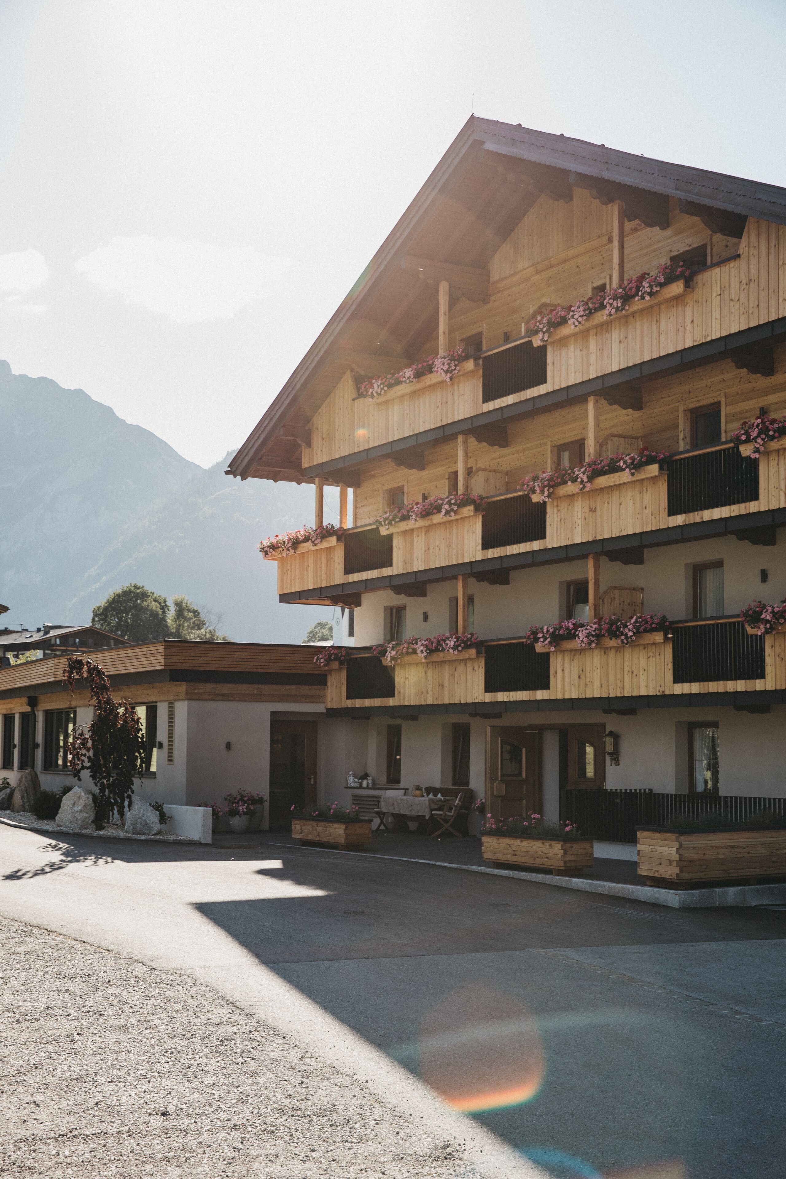 Un edificio de madera de varios pisos con balcones decorados con flores, con montañas al fondo.
