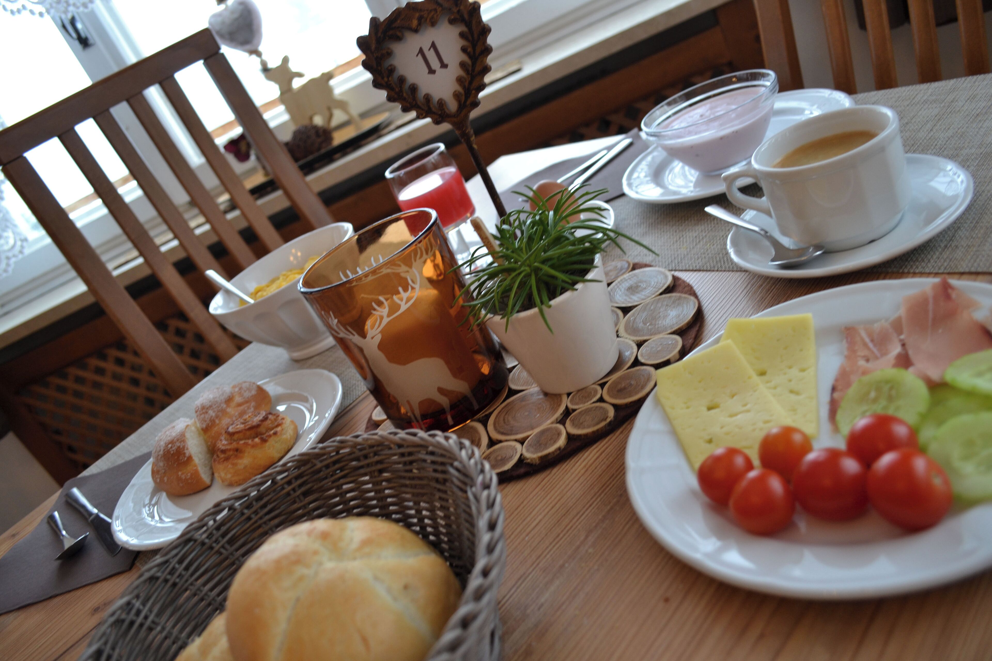 A table set with breakfast items including bread, cheese, tomatoes, and a plant.