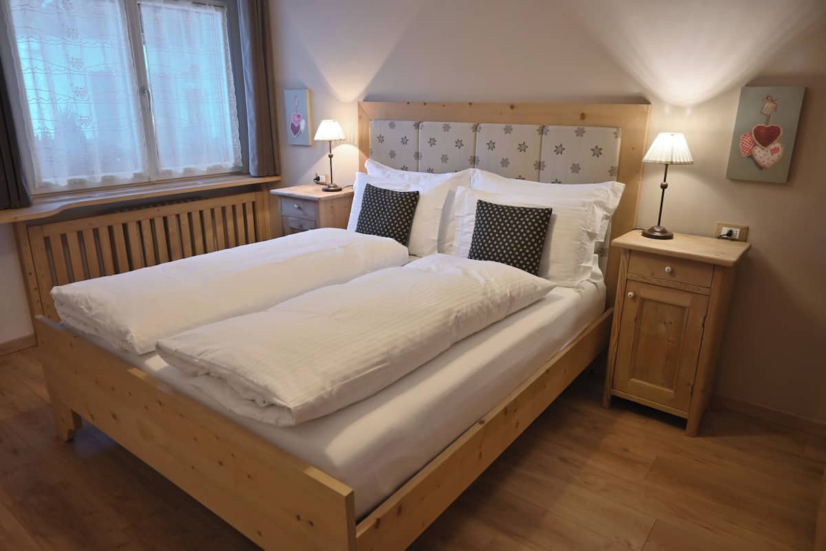 Ein Doppelbett mit Holzrahmen, zwei Nachttische mit Lampen, ein Fenster mit Spitzenvorhängen und eine Wand mit Herzdeko.