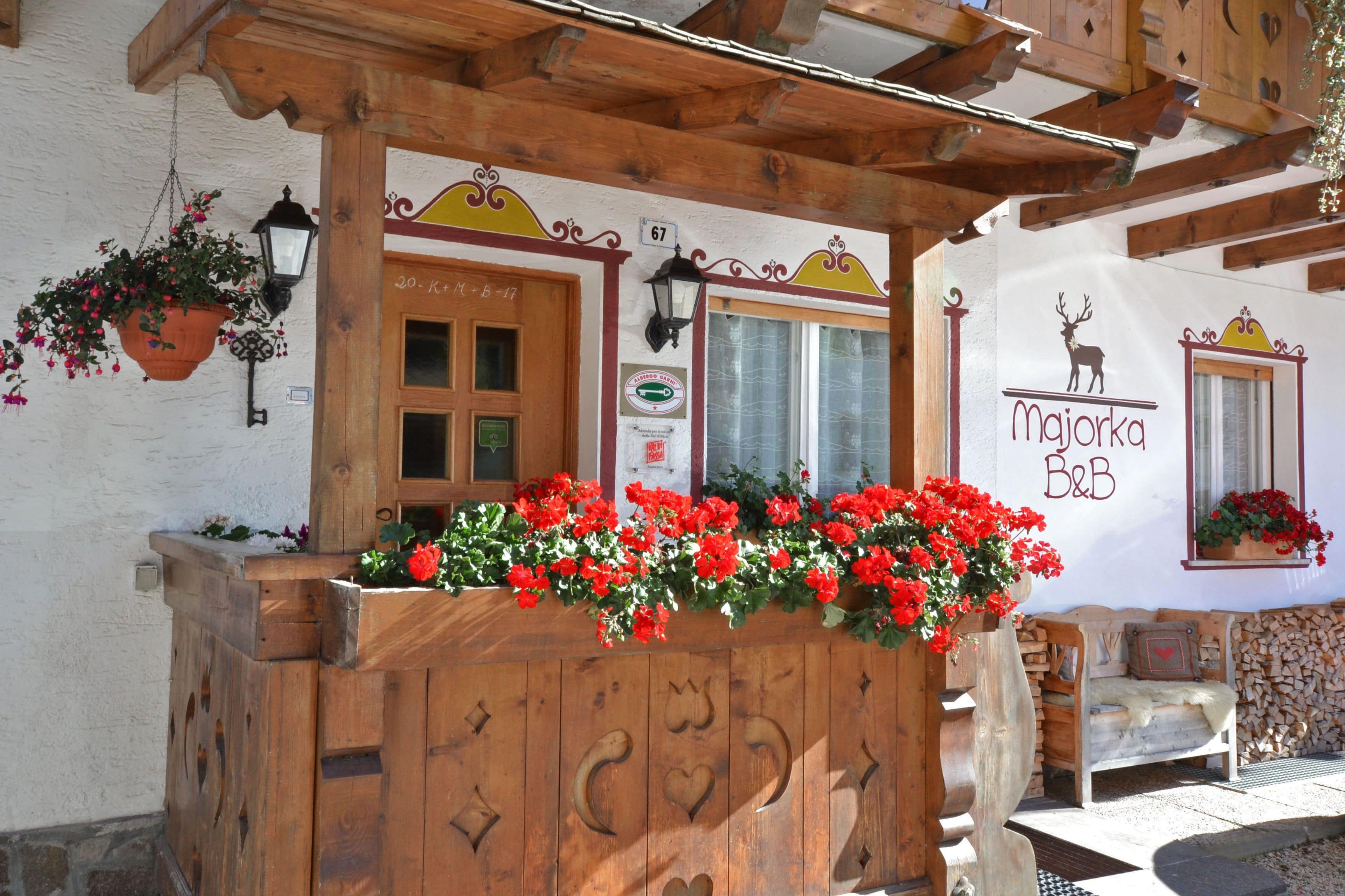 A wooden bench with carved designs, a flower box with red flowers, and a sign with a deer and the text "Majorka B&B".