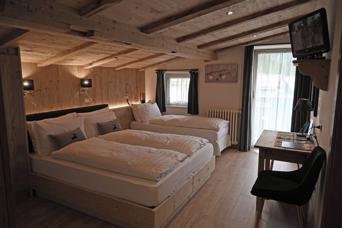 Ein Zimmer mit zwei Betten, einer Holzbalkendecke, einem Tisch mit Stuhl und einem Fernseher auf einem Schrank.