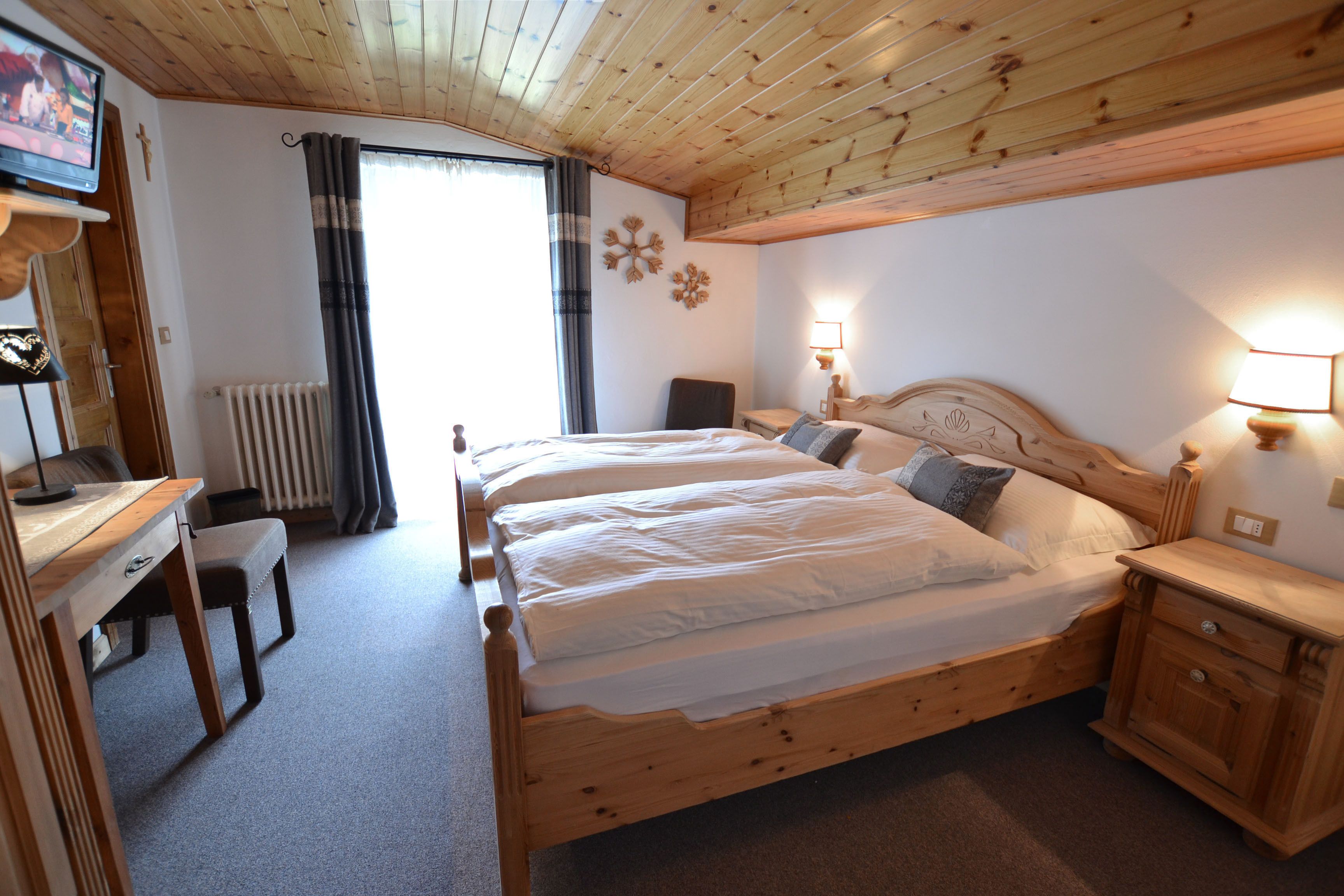 A wooden bedroom with two beds, a desk, and a chair.