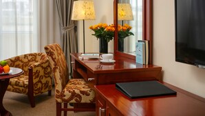 Une chambre d’hôtel avec un bureau en bois, une chaise, un vase de fleurs, une lampe, un téléviseur et un panier de fruits.
