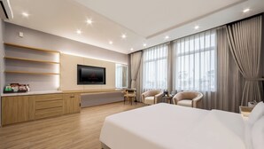 Une chambre d’hôtel moderne dotée d’un grand lit, d’un téléviseur à écran plat fixé au mur, d’un bureau avec une chaise et d’un coin salon avec deux fauteuils.