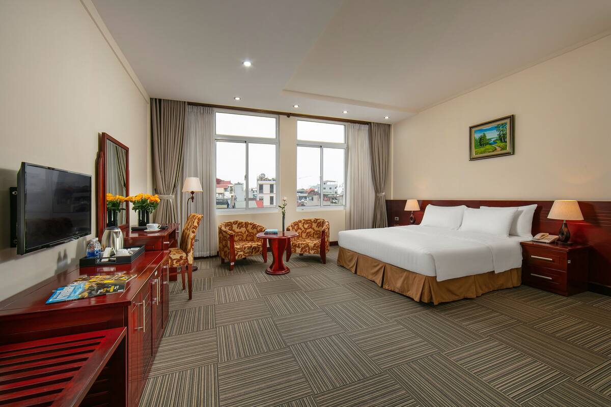 A hotel room with a bed, desk, TV, and a view of the city.