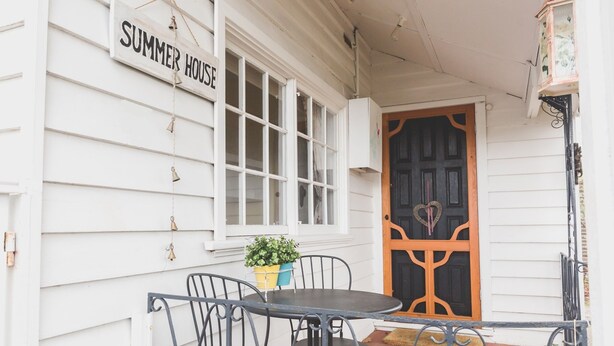Un bâtiment blanc avec une enseigne indiquant « SUMMER HOUSE », une porte noire ornée d’un motif en forme de cœur et une petite table avec des chaises à l’extérieur.