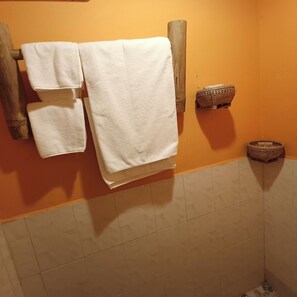 A bathroom with a wooden towel rack holding three white towels, a woven basket on the wall, and a tiled floor. - Siem Reap Homesteading (Siem Reap)