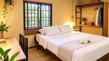 Un dormitorio ordenado con cama, mesitas de noche, un estante con ropa y plantas en macetas.