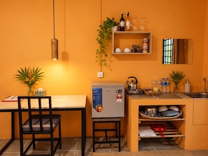 Une cuisine compacte équipée d’un réfrigérateur, d’une bouilloire et d’un évier. On y trouve deux chaises et une petite table.