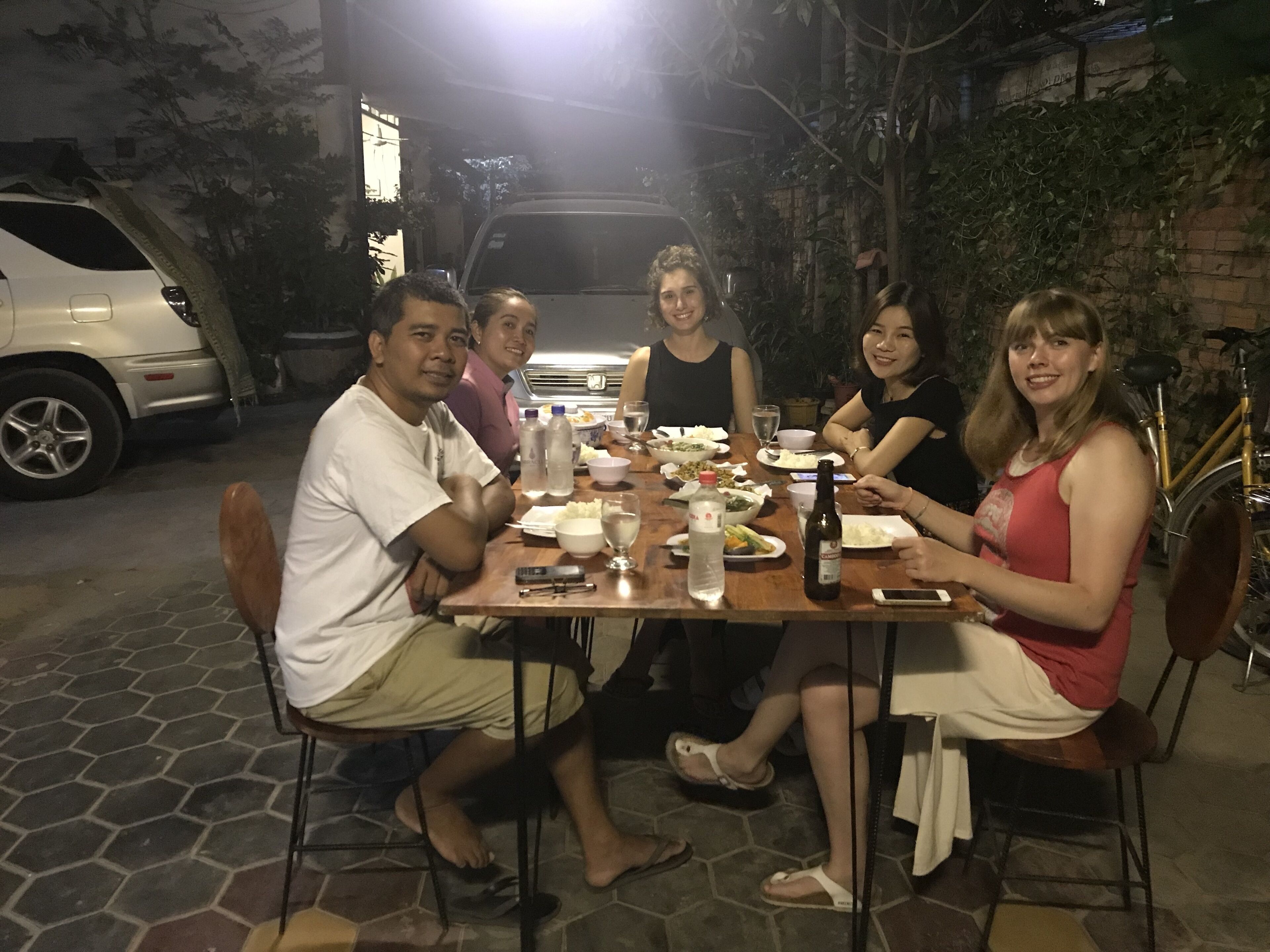 A group of people dining at an outdoor table with a variety of dishes and drinks.