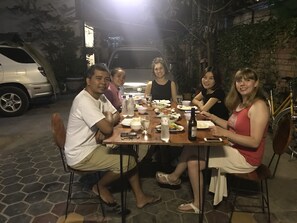 Um grupo de pessoas jantando em uma mesa ao ar livre, com diversos pratos e bebidas.
