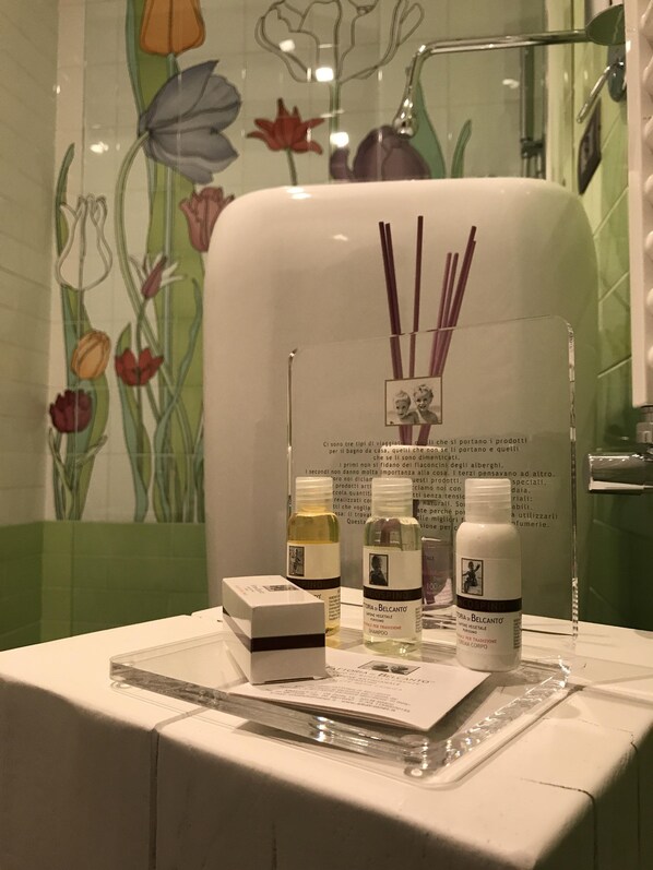 A bathroom with a floral tile backsplash, a shower area, and a vanity with toiletries and a brochure. - Fonte Gaia Experience B&B (Siena)