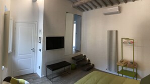 A bedroom with a wooden ceiling, a bed, a bench, a mirror, a radiator, and a shelf with towels. - Fonte Gaia Experience B&B (Siena)