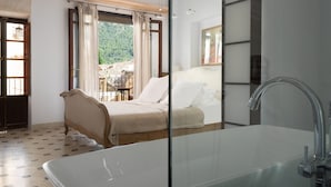 A bedroom with a large bed, a glass-enclosed bathroom, and a view of a balcony with outdoor furniture. - Mallorca One by Balearic Villas (Pollensa)