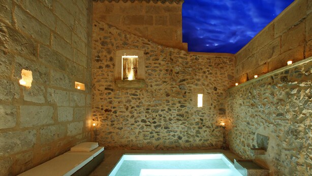 A stone-walled room with a glass-enclosed hot tub, a small window, and wall-mounted lights. - Mallorca One by Balearic Villas (Pollensa)