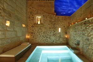A stone-walled room with a glass-enclosed hot tub, a small window, and wall-mounted lights. - Mallorca One by Balearic Villas (Pollensa)