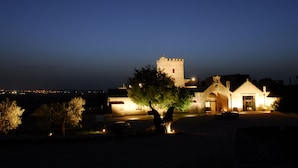 A castle-like building with a tower, illuminated by warm lights, surrounded by trees and a parked car. - Masseria Torre Spagnola  (Matera)