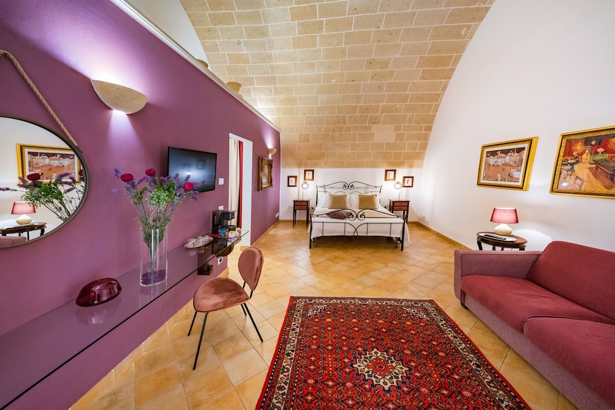 A bedroom with a bed, a sofa, a chair, a TV, and a mirror.