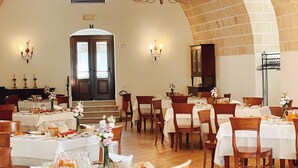 A spacious dining area with multiple tables and chairs, a chandelier, and a high arched ceiling. - Masseria Torre Spagnola  (Matera)