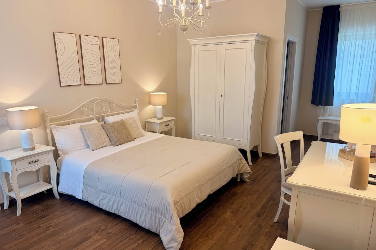 A neatly arranged bedroom with a bed, bedside tables, a wardrobe, and a desk with a lamp.