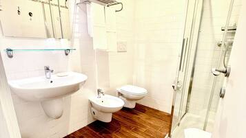 Een badkamer met een wastafel, toilet, douchecabine en een bidet.