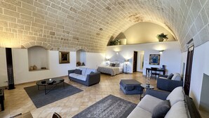 A spacious living area with a high arched ceiling, a sofa set, a bed, and a small table with a chair. - Masseria Torre Spagnola  (Matera)