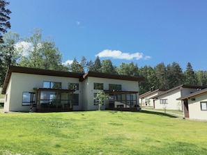 A modern two-story building with large windows and a flat roof, surrounded by a well-maintained lawn and trees.