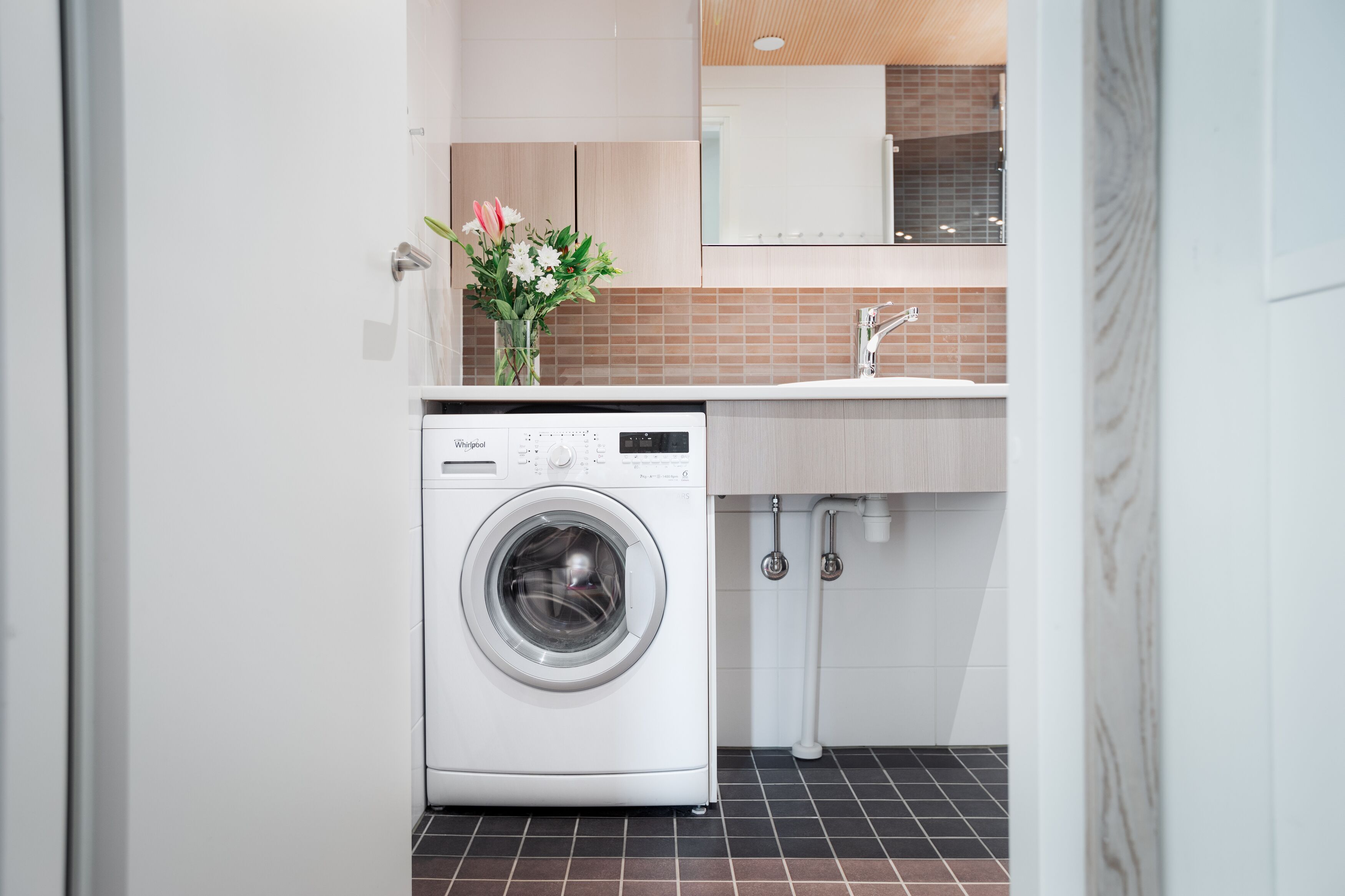 Moderni pyykinhuone, jossa on etuaukollinen Whirlpool-pesukone ja pesuallas, jonka yläpuolella on peili.