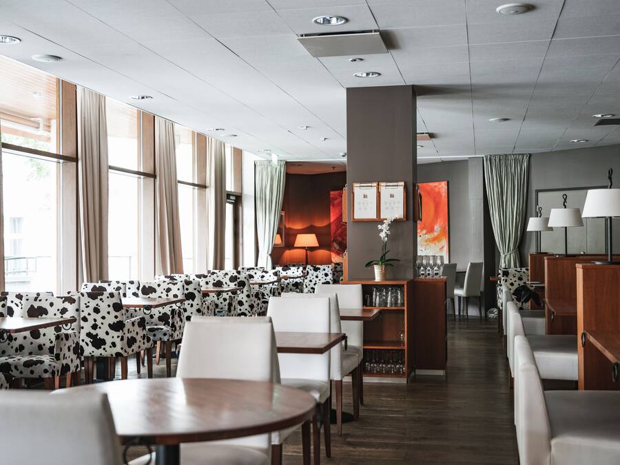 A modern hotel lobby with a seating area featuring cow-print upholstered chairs and tables, a central fireplace, and a view of the outdoors through large windows.
