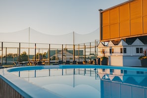 A swimming pool with lounge chairs and a netted area, surrounded by buildings with a modern design.