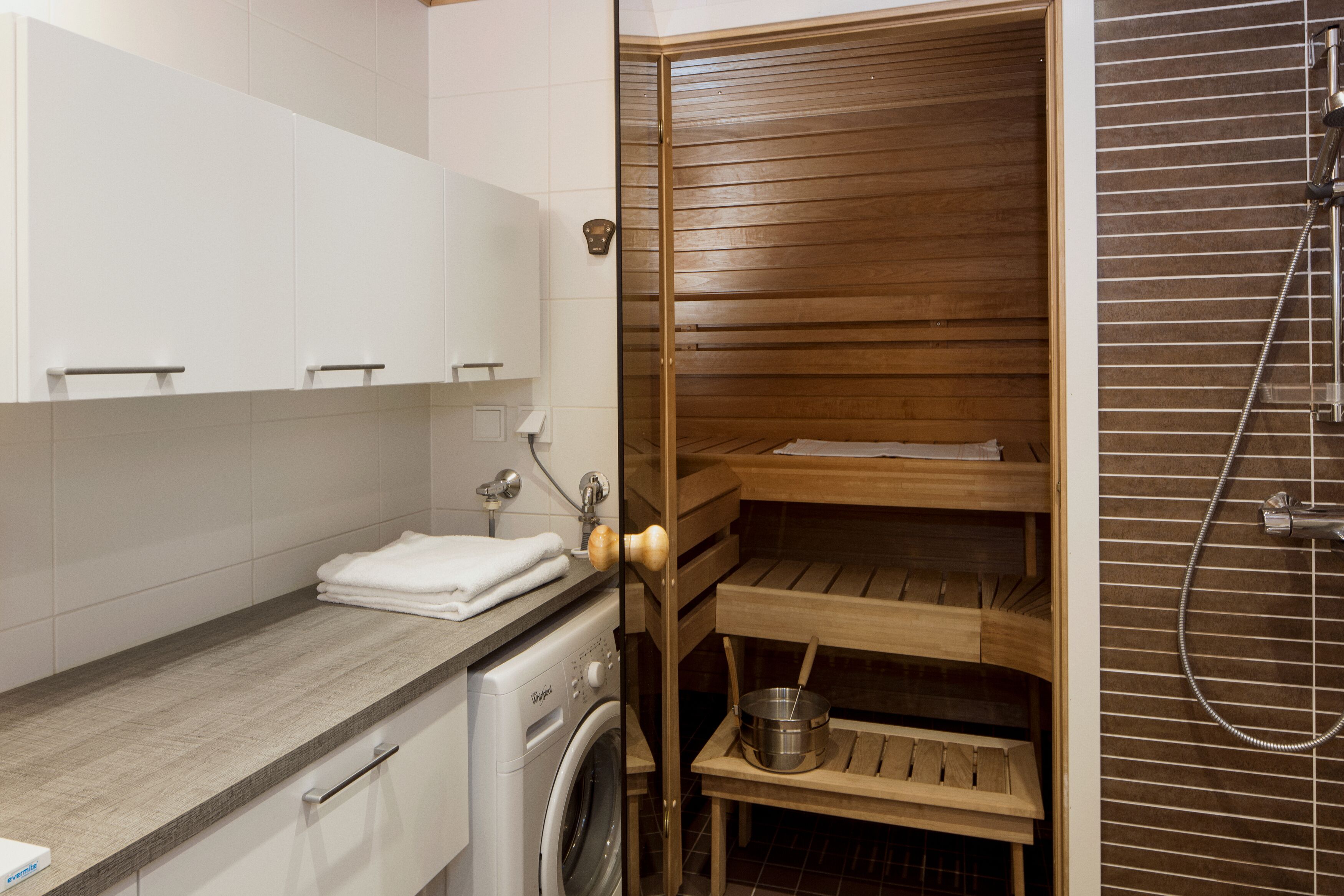 Un baño pequeño con lavadora, repisas de madera y zona de ducha.