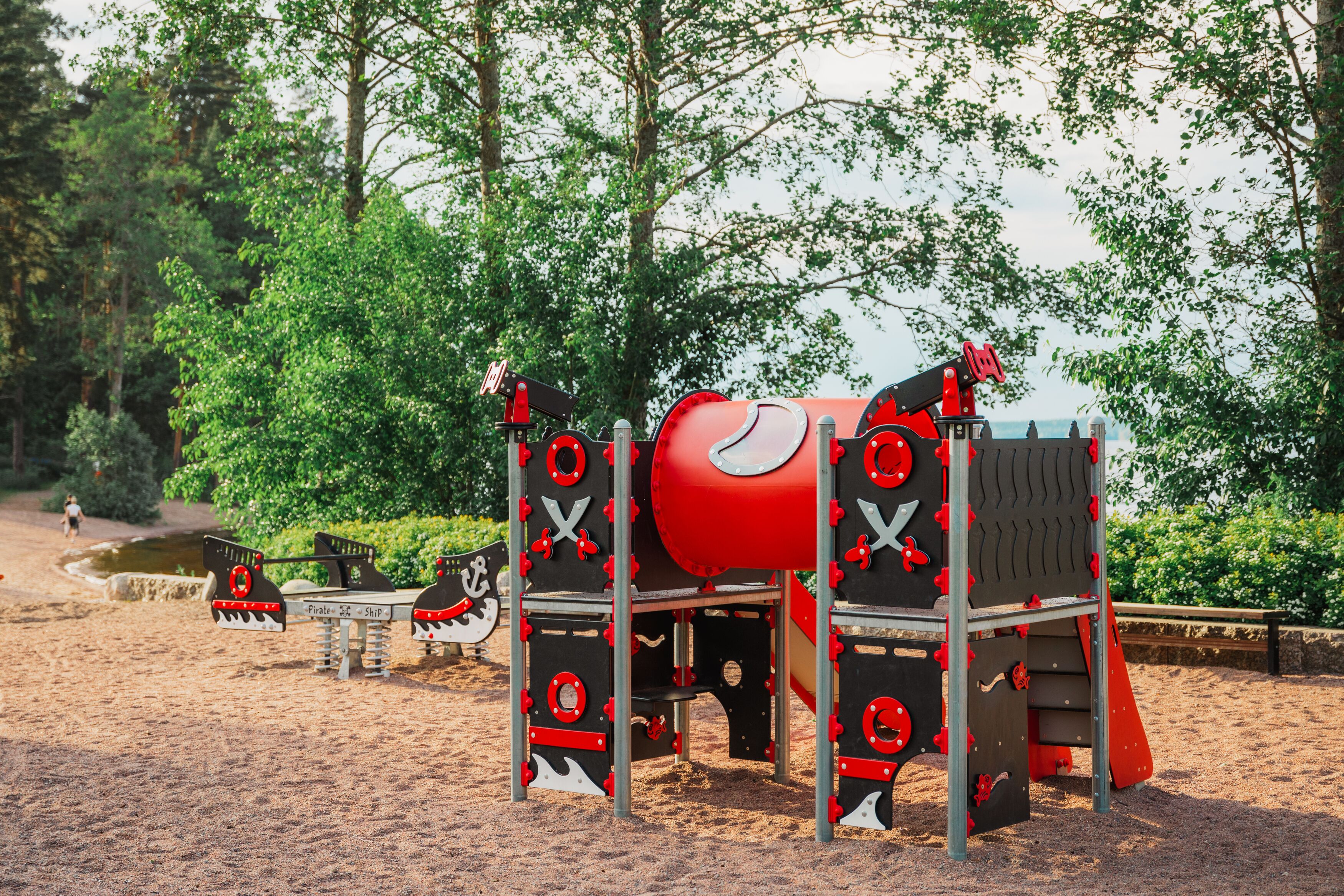 A pirate-themed playground with slides and climbing structures, surrounded by trees and a sandy ground.