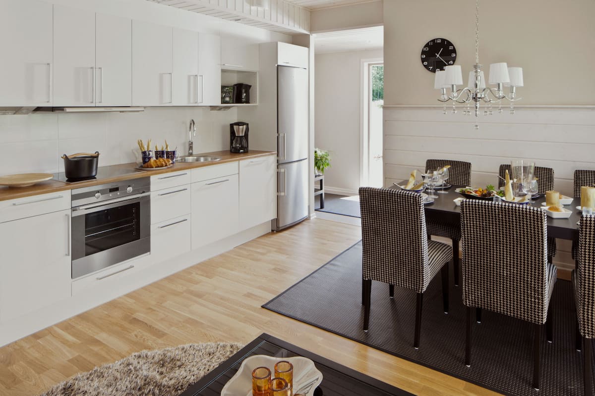 Une cuisine moderne avec des armoires blanches, un réfrigérateur en acier inoxydable et un coin repas avec des chaises à carreaux et une table dressée pour quatre personnes.