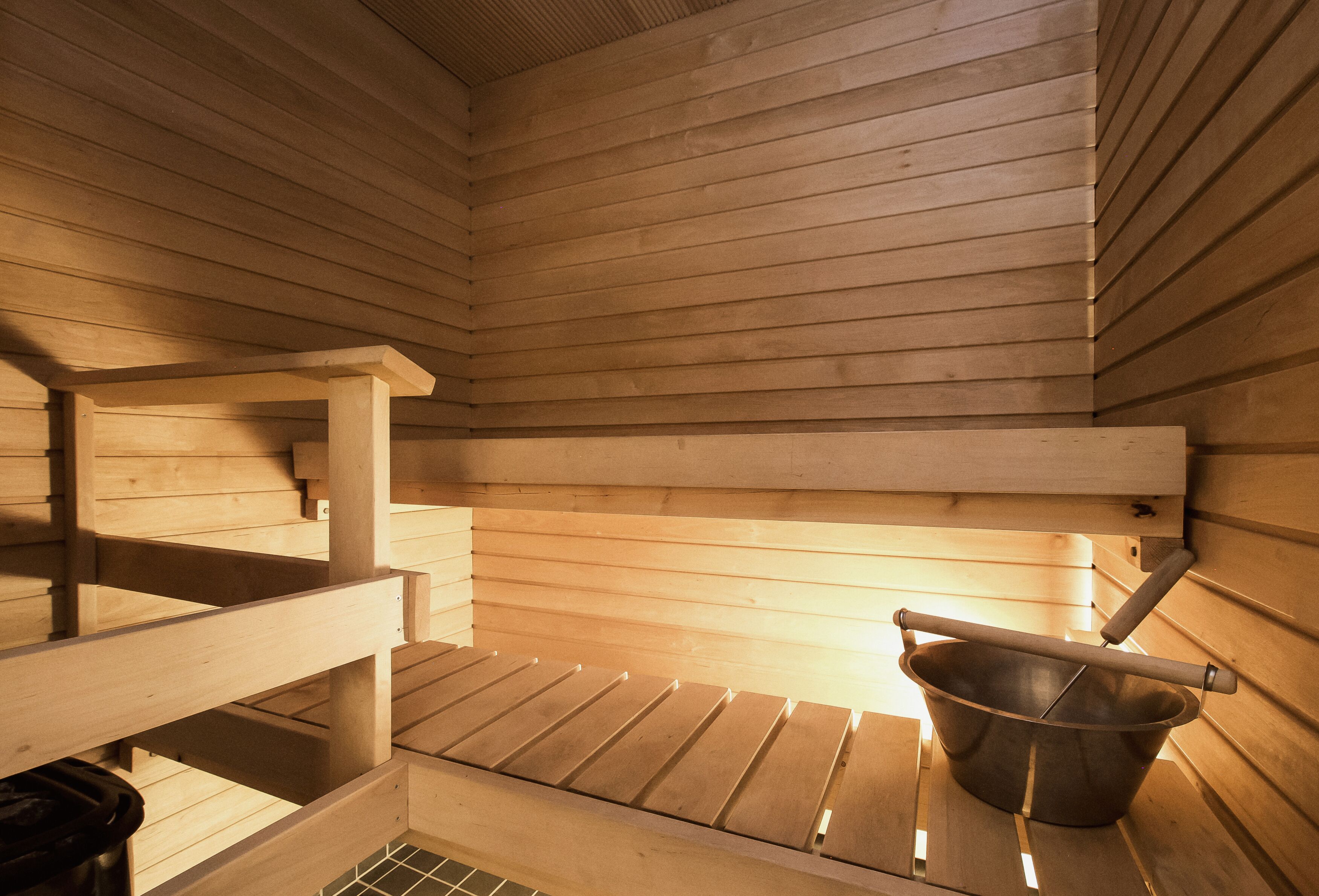 Sauna, jossa on puiset lauteet ja metallinen ämpäri.