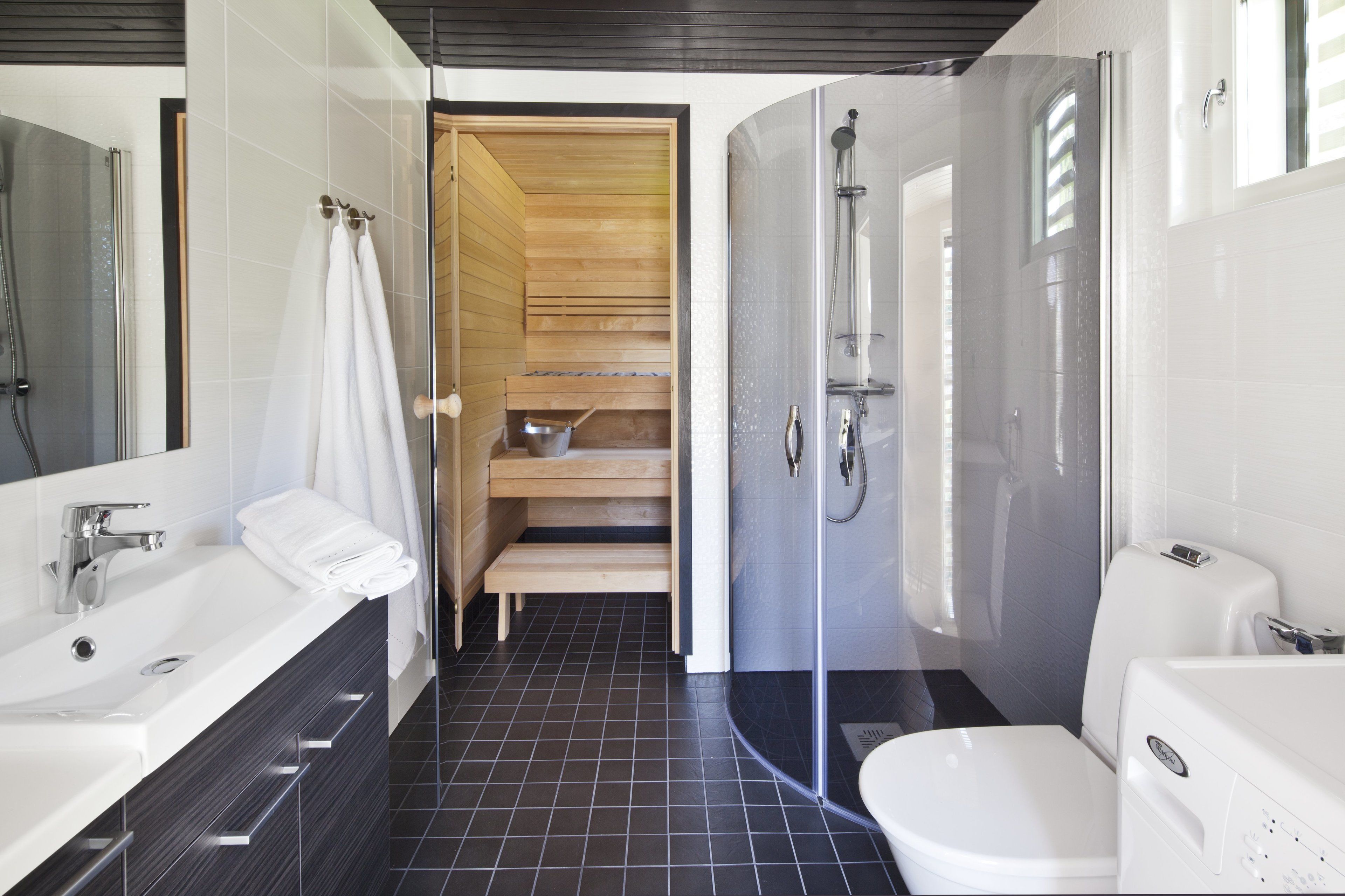 Ein modernes Badezimmer mit einem großen weißen Waschbecken, einer separaten Toilette, einer gläsernen Dusche und einer Holzsauna.