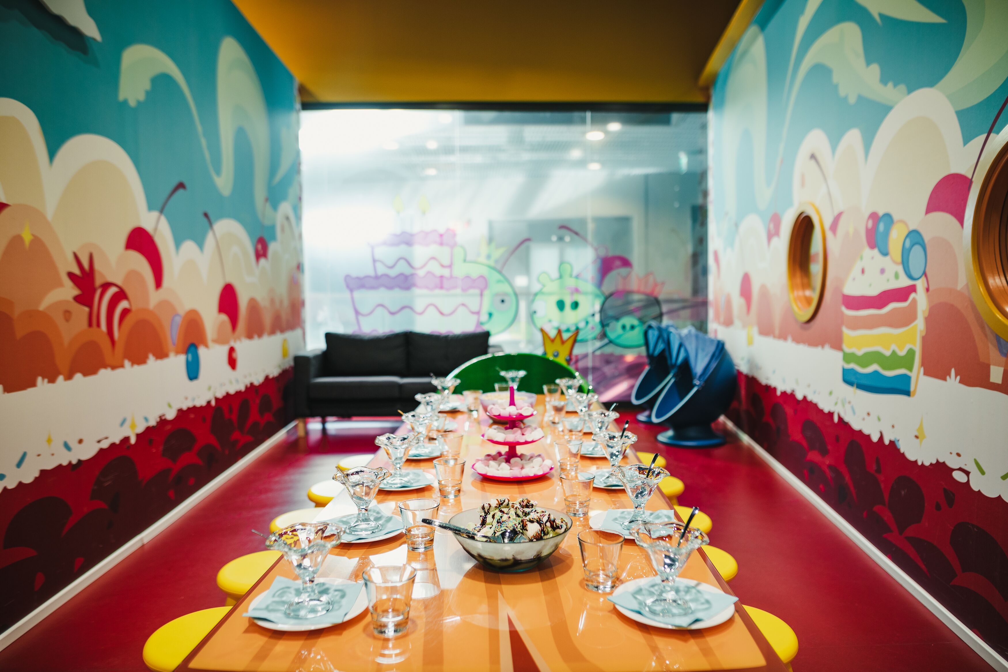 A long table set for a meal with colorful wall art and a bright red floor.