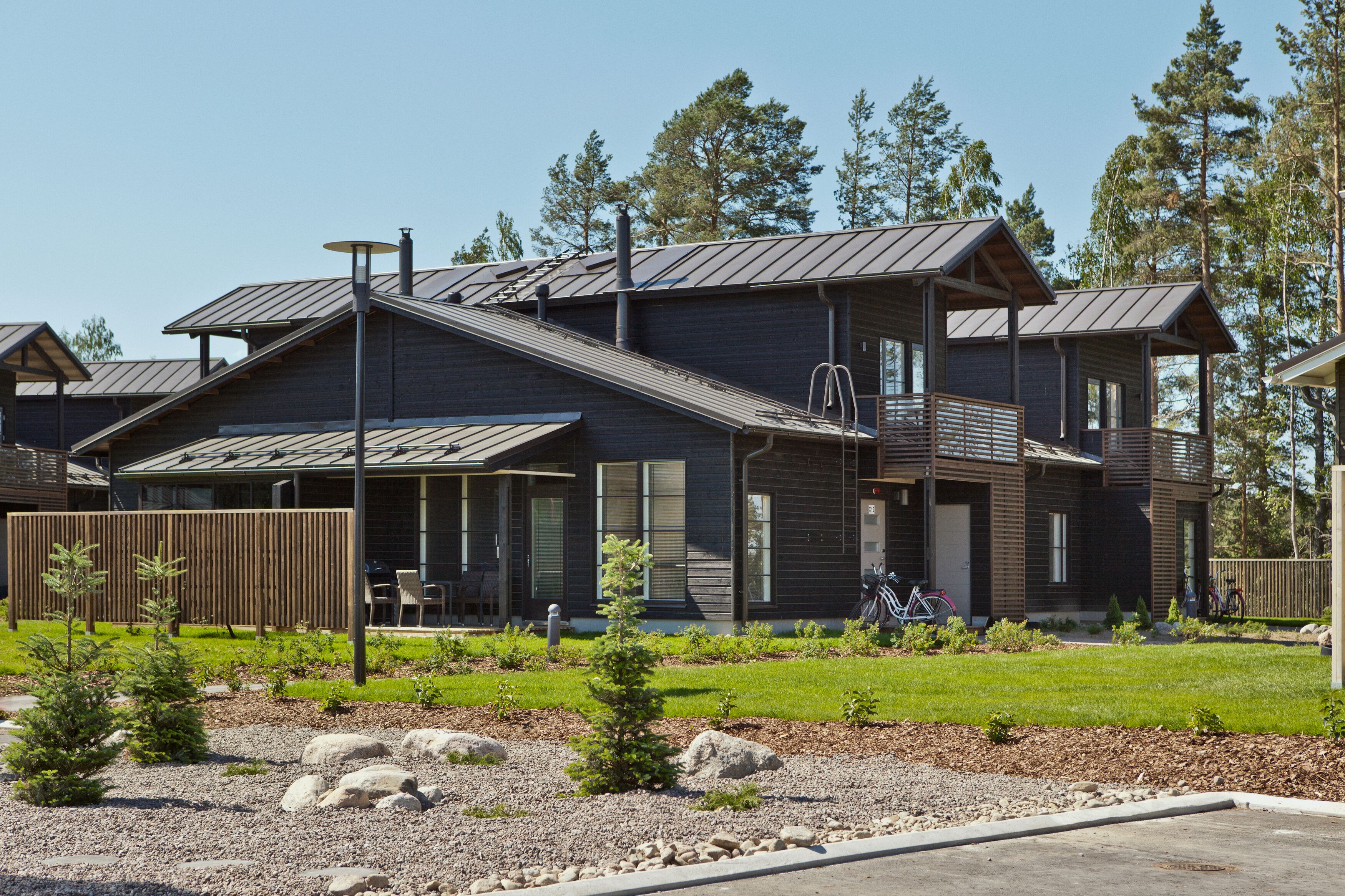 A modern two-story house with a covered porch, a metal roof, and a well-maintained garden with rocks and small trees.