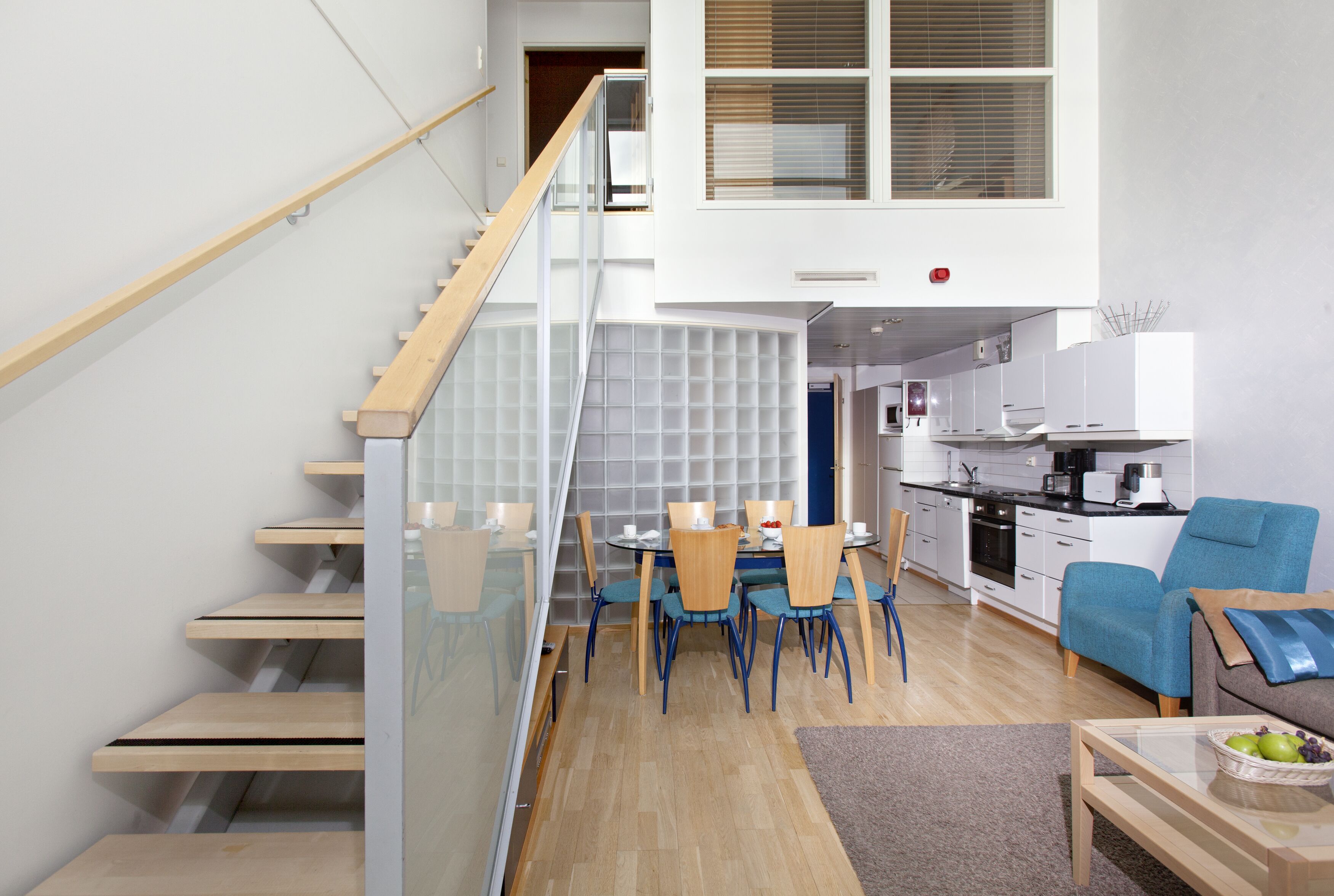 A modern apartment with a staircase, a dining area, a kitchen, and a living room.